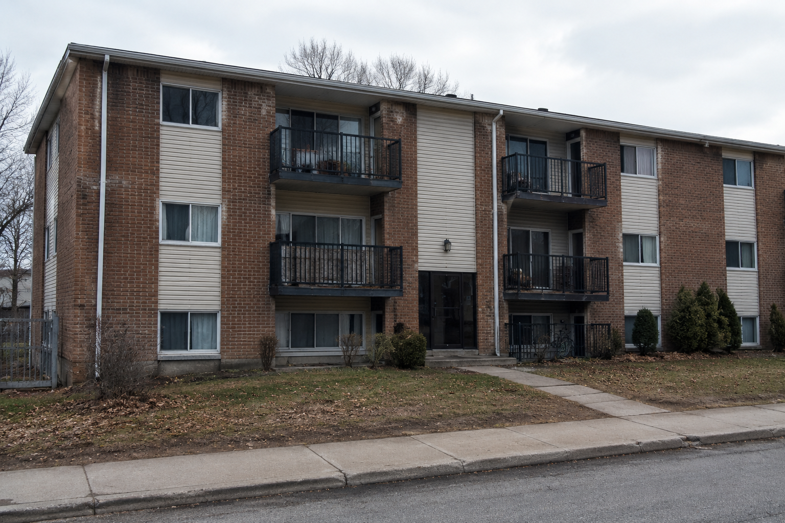 Apartment building exterior showing overgrown shrubs near entrance, worn details and dirty walkways — before improvements